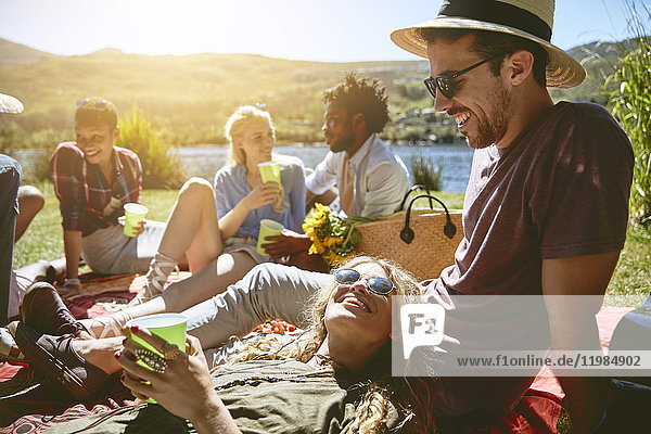Junge Freunde entspannen sich  genießen ein Picknick am sonnigen Sommerufer des Flusses.