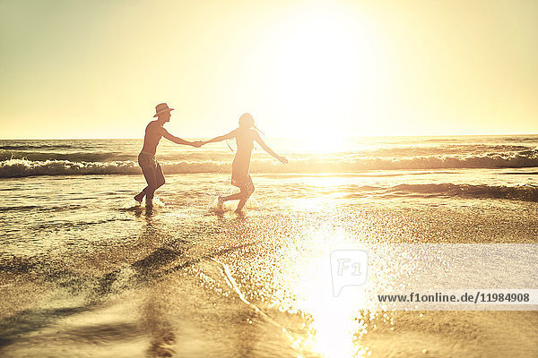Junges Paar hält sich an den Händen  wandert im sonnigen Sommer bei Sonnenuntergang am Strand.
