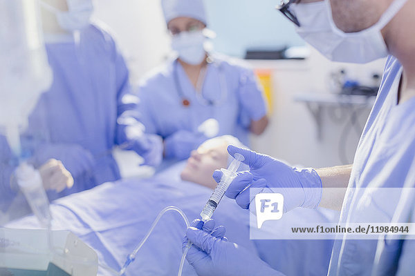 Anästhesist mit Spritze beim Einspritzen von Narkosemitteln in den IV-Tropf im Operationssaal