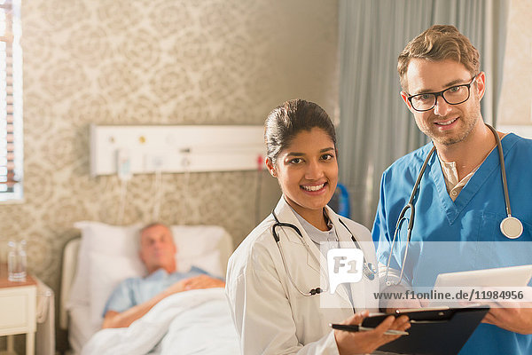 Porträt eines lächelnden  selbstbewussten Arztes und einer Krankenschwester bei der Visite  die ein digitales Tablet und ein Klemmbrett in einem Krankenhauszimmer benutzen