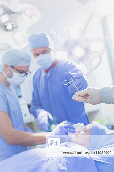 Chirurg greift im Operationssaal nach einer chirurgischen Schere