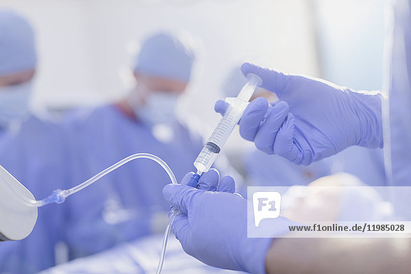 Nahaufnahme eines Anästhesisten mit einer Spritze  der Narkosemittel in einen IV-Tropf im Operationssaal injiziert