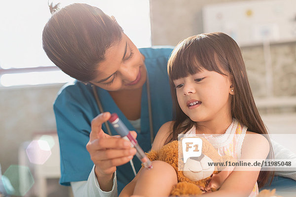 Krankenschwester bringt einem Mädchen mit Teddybär bei  wie man einen Insulin-Pen benutzt