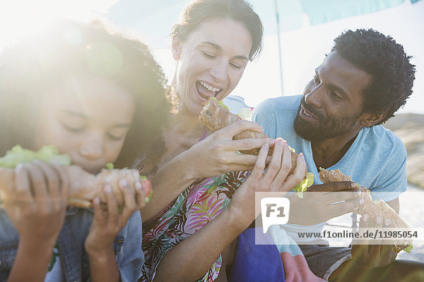 Multi-ethnische Familie isst Baguette-Sandwiches am sonnigen Strand