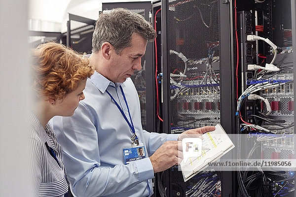 IT technicians with clipboard examining panel in server room