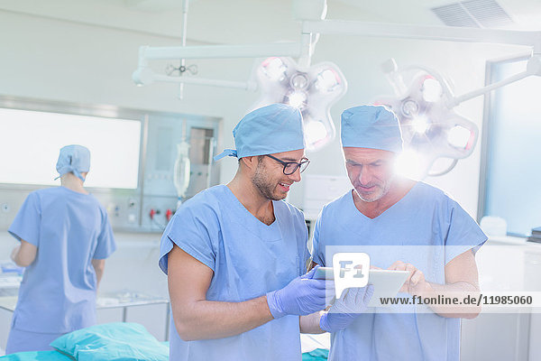 Männliche Chirurgen im Gespräch und mit digitalem Tablet im Operationssaal