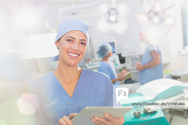 Porträt einer lächelnden  selbstbewussten Chirurgin  die ein digitales Tablet im Operationssaal benutzt