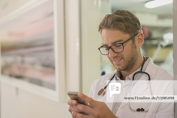 Männlicher Arzt  der mit seinem Handy im Krankenhaus SMS schreibt