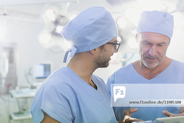 Männliche Chirurgen im Gespräch und mit digitalem Tablet im Operationssaal