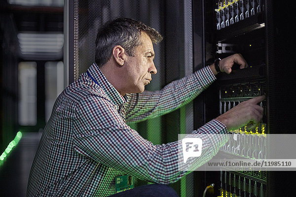 Focused male IT technician working at panel in dark server room