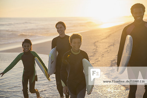 Familien-Surfer beim Wandern mit Surfbrettern am sonnigen Sommer-Sonnenuntergang am Meeresstrand