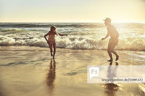 Verspieltes junges Paar  das im nassen Sand am sonnigen Sommerstrand läuft.