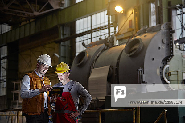 Ingenieur und Arbeiter mit digitalem Tablett in dunkler Fabrik