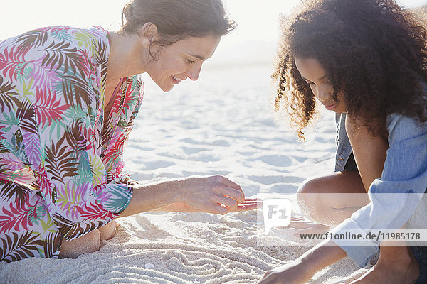 Mutter und Tochter malen im Sand am sonnigen Sommerstrand