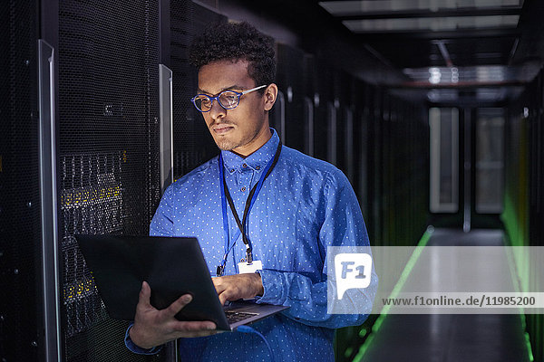 Fokussierter IT-Techniker mit Laptop im dunklen Serverraum