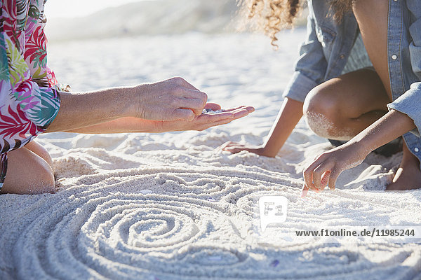 Mutter und Tochter legen Muscheln in Spiralen in Sand am sonnigen Sommerstrand.