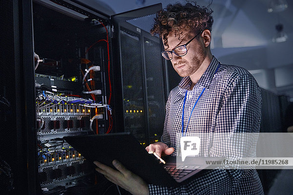 Fokussierter IT-Techniker am Laptop im dunklen Serverraum