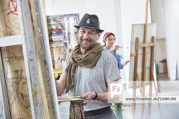 Portrait smiling male artist painting at easel in art class studio