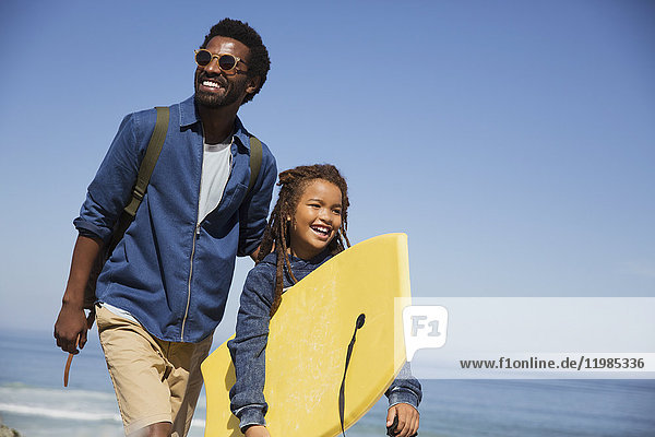 Lächelnder Vater und Tochter mit Boogie-Board am sonnigen Sommerstrand des Ozeans