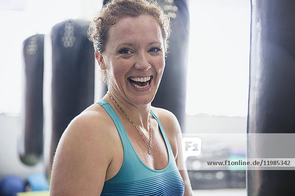 Portrait laughing female boxer standing at punching bag in gym