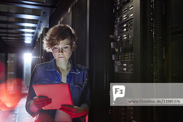 Focused female IT technician using digital tablet in server room