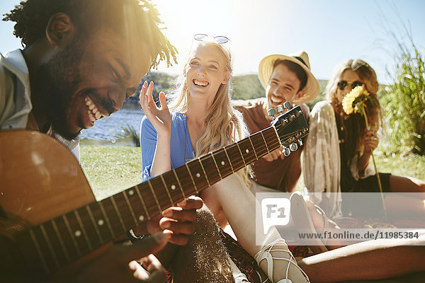Junge Freunde lachen und Gitarre spielen,  sonniges Sommerpicknick genießen