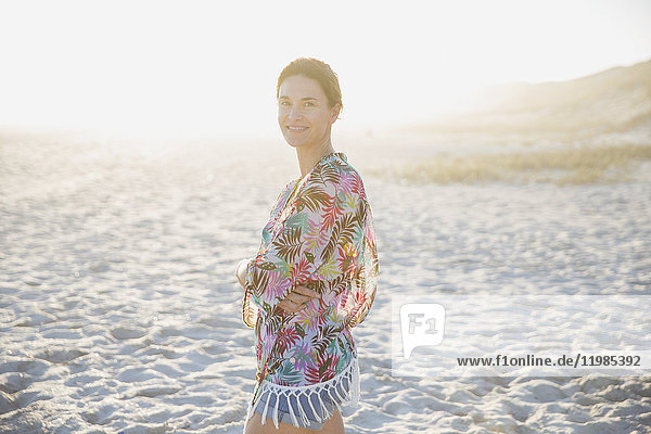 Portrait lächelnde  selbstbewusste  brünette Frau im Badeanzug am sonnigen Sommer-Sonnenuntergangstrand.