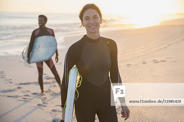 Portrait selbstbewusste Frau im Neoprenanzug mit Surfbrett am sonnigen Sommerstrand mit Familie