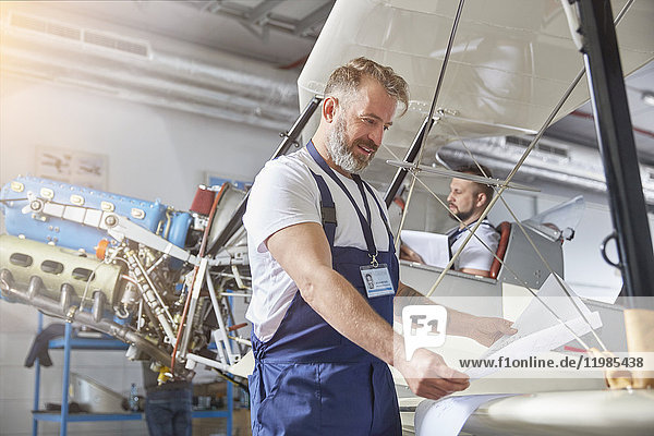 Männlicher Maschinenbauingenieur bei der Überprüfung von Plänen am Flugzeug im Hangar
