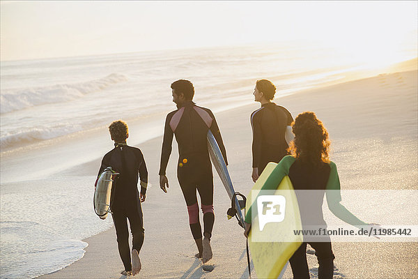 Familienwandern mit Surfbrettern und Boogie-Board am sonnigen Sommer-Sonnenuntergangsstrand