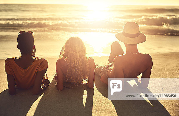 Unbeschwerte junge Freunde  die sich am sonnigen Sommer-Sonnenuntergang am Meer entspannen.