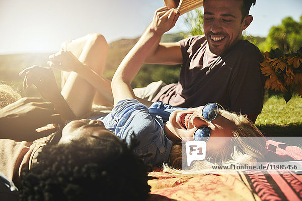 Verspielte junge Freunde lachend  entspannend auf Picknickdecke im sonnigen Sommerpark