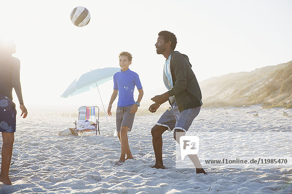 Vater und Kinder spielen Fußball am sonnigen Sommerstrand