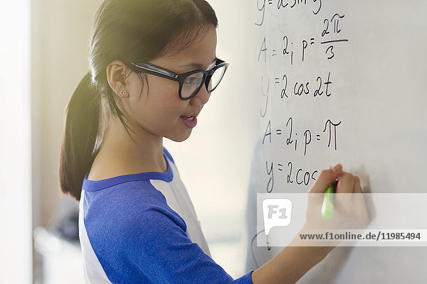 Portrait lächelndes  selbstbewusstes Mädchen  das Physikgleichungen am Whiteboard im Klassenzimmer löst.