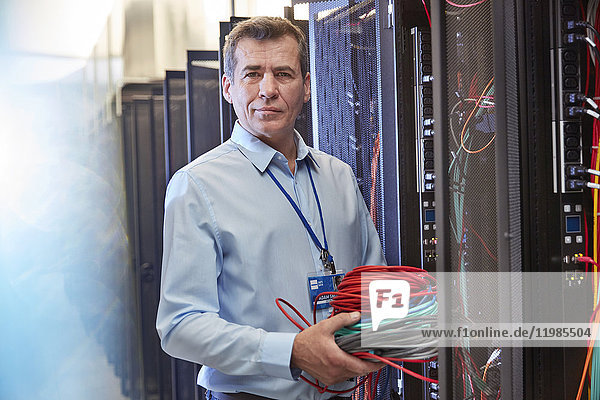 Portrait serious male IT technician holding cables in server room