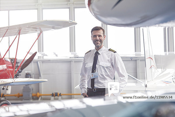 Porträt eines lächelnden Piloten in der Nähe des Flugzeugs im Hangar