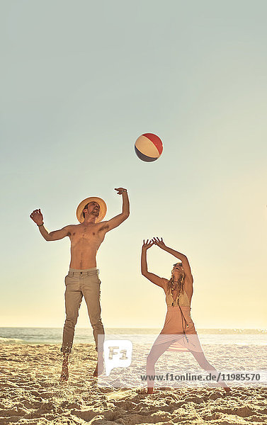 Junges Paar spielt mit Strandball am sonnigen Sommerstrand