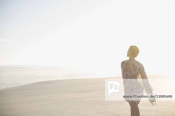 Serene woman in swimsuit coverup walking on sunny summer beach