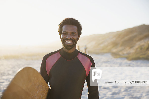 Portrait smiling  confident male surfer with surfboard on sunny summer beach