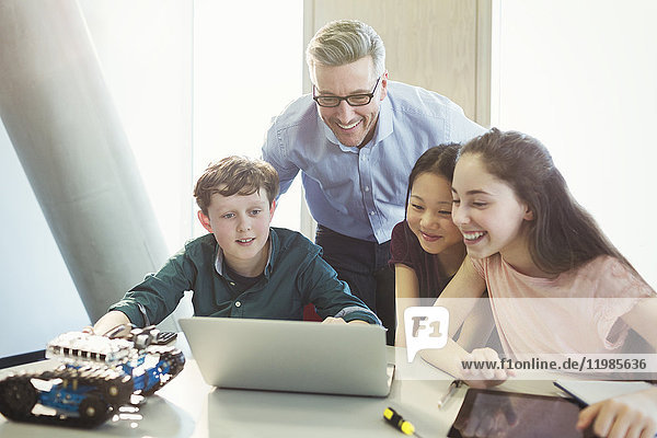 Lächelnder Lehrer und Schüler beim Programmieren von Robotik am Laptop im Klassenzimmer