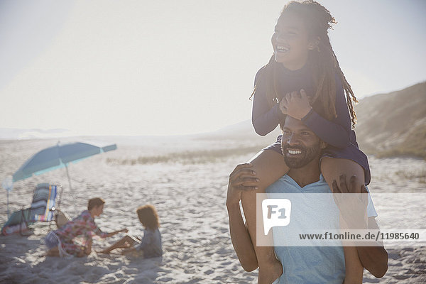 Smiling father carrying daughter on shoulders on sunny summer beach