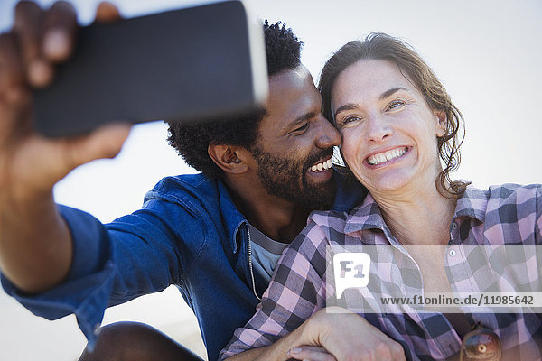 Lächelndes  enthusiastisches multiethnisches Paar  das Selfie mit Fotohandy nimmt.