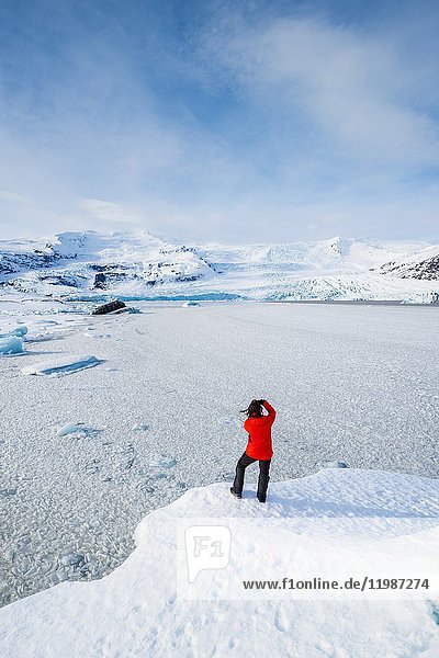 Gletscherlagune Fjallsarlon  Ostisland  Island. Mann mit rotem Mantel bewundert die Aussicht auf die zugefrorene Lagune im Winter (MR).