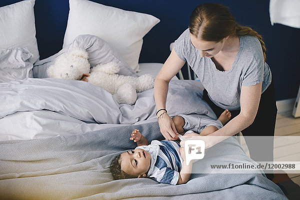 Mutter beim Ankleiden Baby Junge auf Bett zu Hause