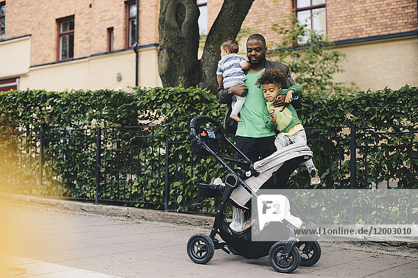 Vater mit Kindern beim Kinderwagen auf dem Bürgersteig in der Stadt