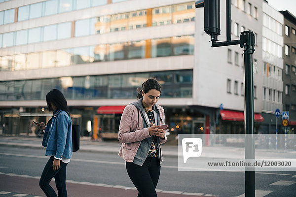 Females walking on sidewalk while using smart phone against building in city