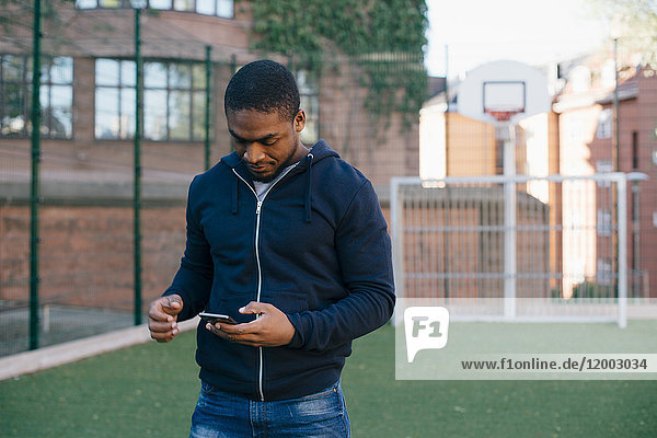 Junger Mann steht auf dem Spielfeld  während er ein Smartphone benutzt.