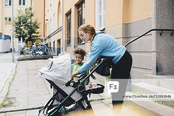 Smiling mother and son looking at baby stroller outside apartment