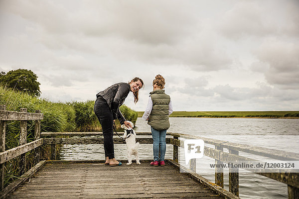 Mutter und Tochter stehen auf einem Steg am See mit Hund