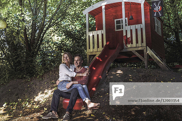 Glückliches Paar sitzt auf der Rutsche eines Gartenschuppens im Wald